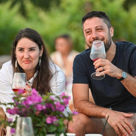 Due persone sorridenti brindano all'aperto con calici di vino.