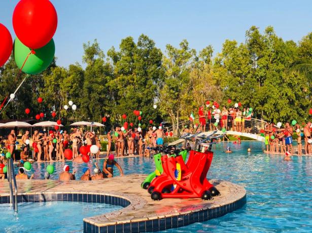 Festa in piscina con palloncini colorati e molte persone.