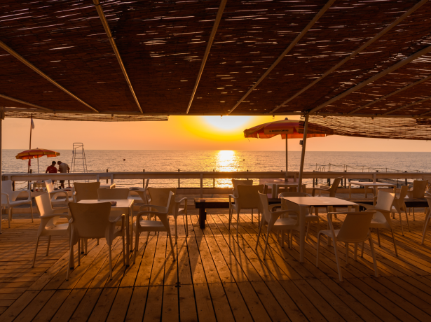 Tramonto su una terrazza con vista mare, sedie e ombrelloni.