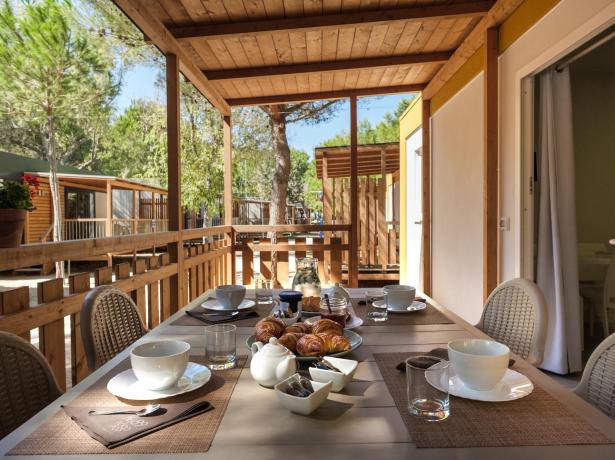 Colazione all'aperto su veranda in legno, circondata da alberi.