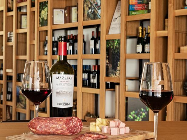Vino rosso con formaggi e salumi su un tagliere di legno.