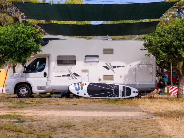 Camper parcheggiato con una tavola da paddle sotto una tettoia.