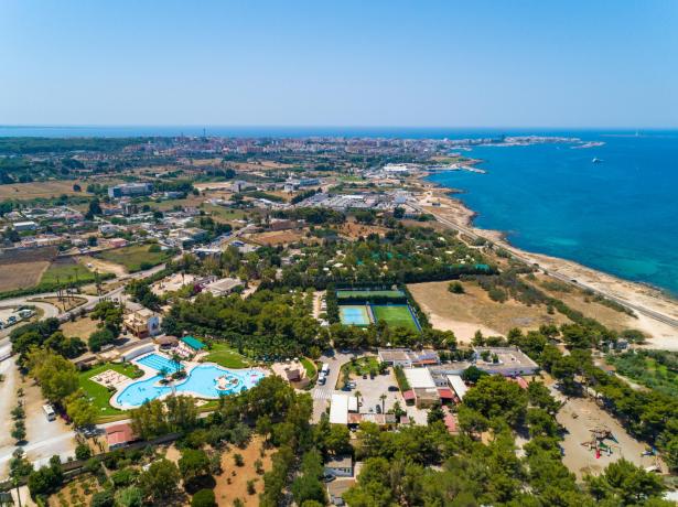 Vista aerea di una città costiera con piscina, campi sportivi e mare.