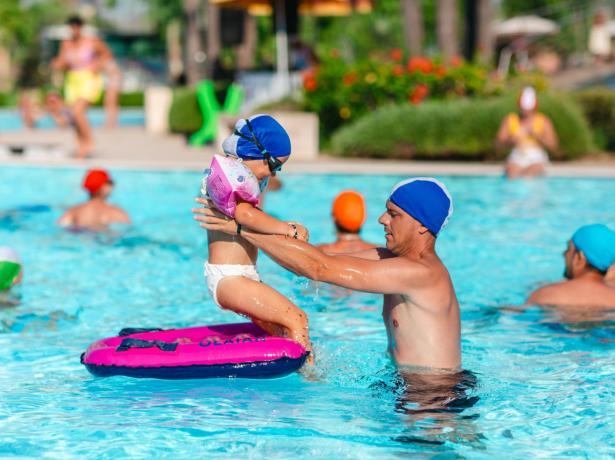 Bambino e adulto giocano in piscina con cuffie colorate.