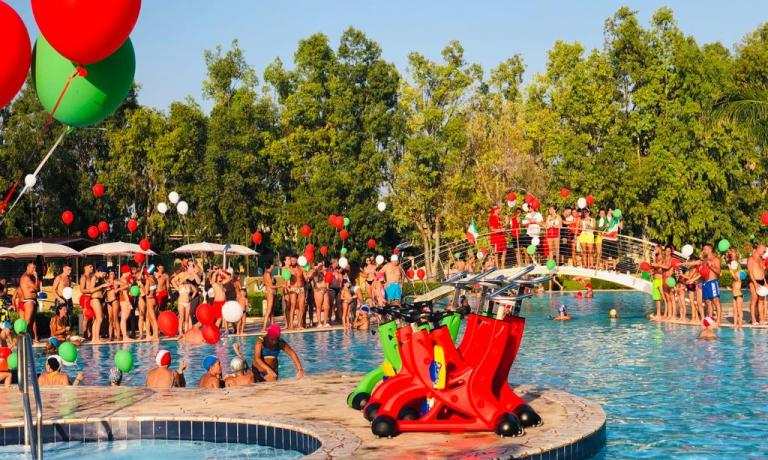 Festa in piscina con palloncini colorati e molte persone.