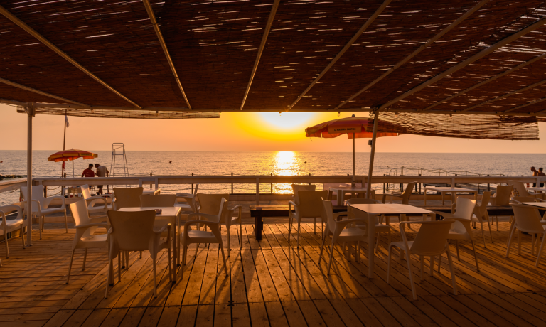 Tramonto su una terrazza con vista mare, sedie e ombrelloni.
