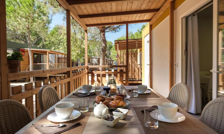 Colazione all'aperto su veranda in legno, circondata da alberi.