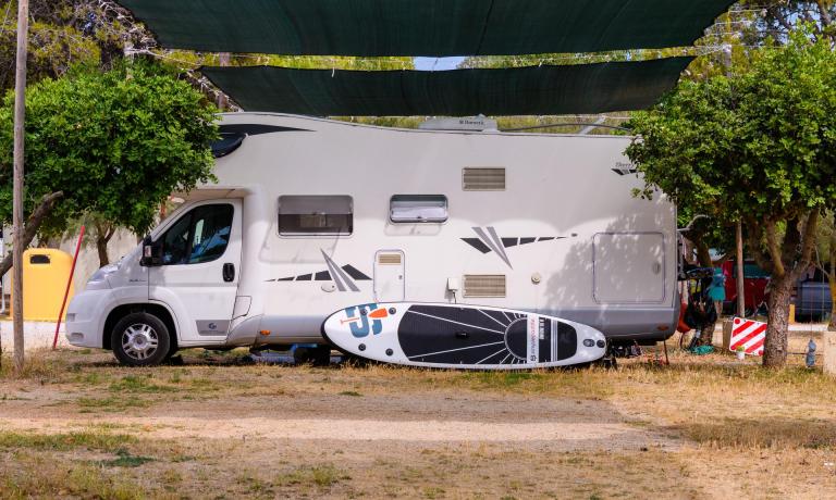 Camper parcheggiato con una tavola da paddle sotto una tettoia.