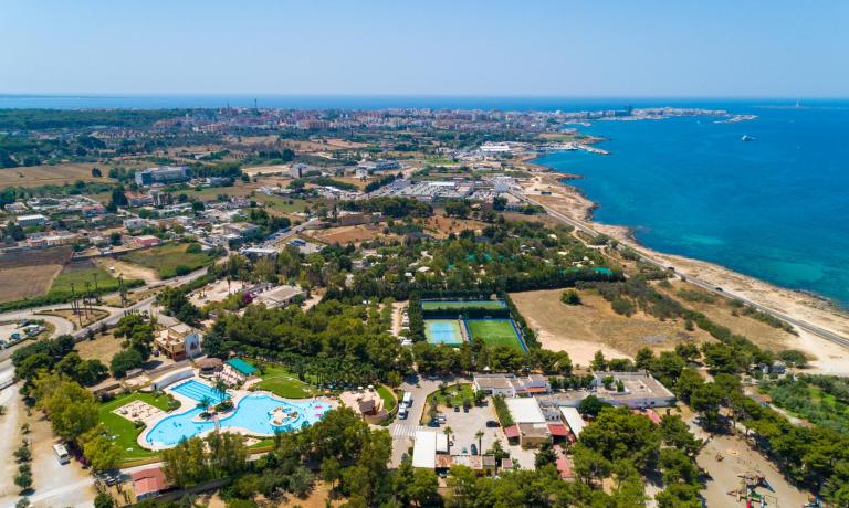 Vista aerea di una città costiera con piscina, campi sportivi e mare.