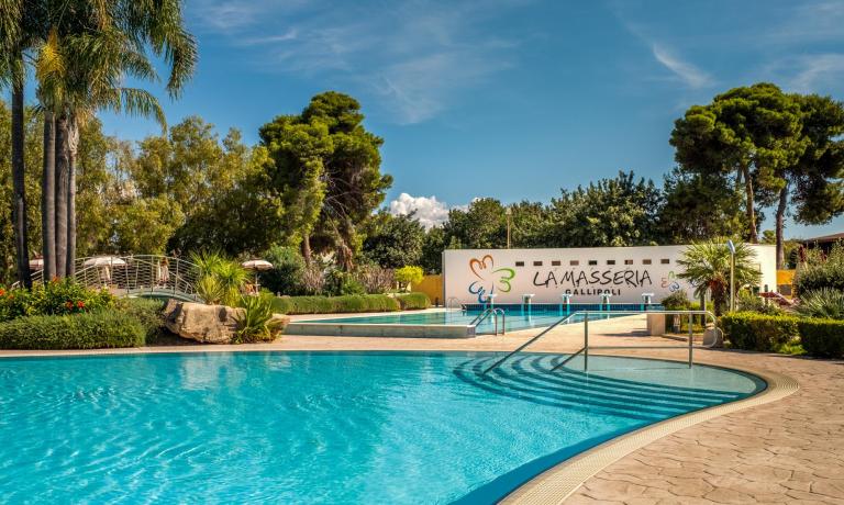 Piscina all'aperto a La Masseria Gallipoli, circondata da palme e giardini.