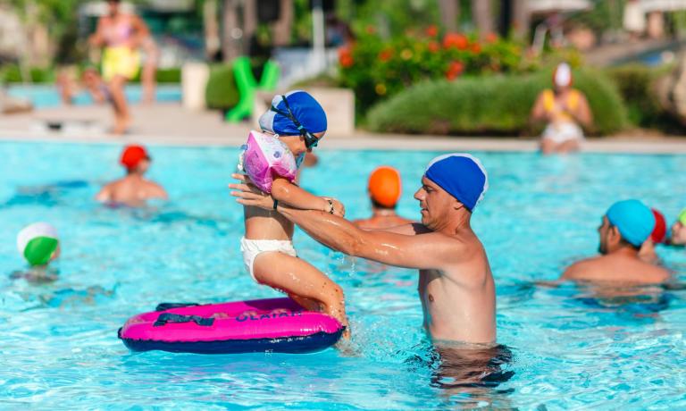 Bambino e adulto giocano in piscina con cuffie colorate.