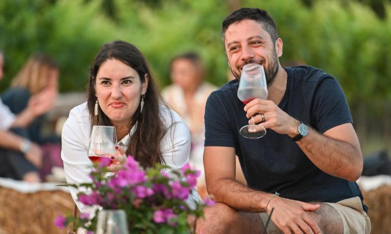 Due persone sorridenti brindano all'aperto con calici di vino.